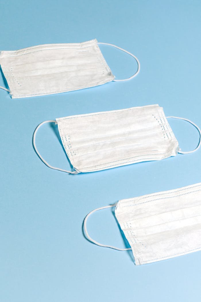 Three white face masks arranged on a pastel blue background, symbolizing health protection.